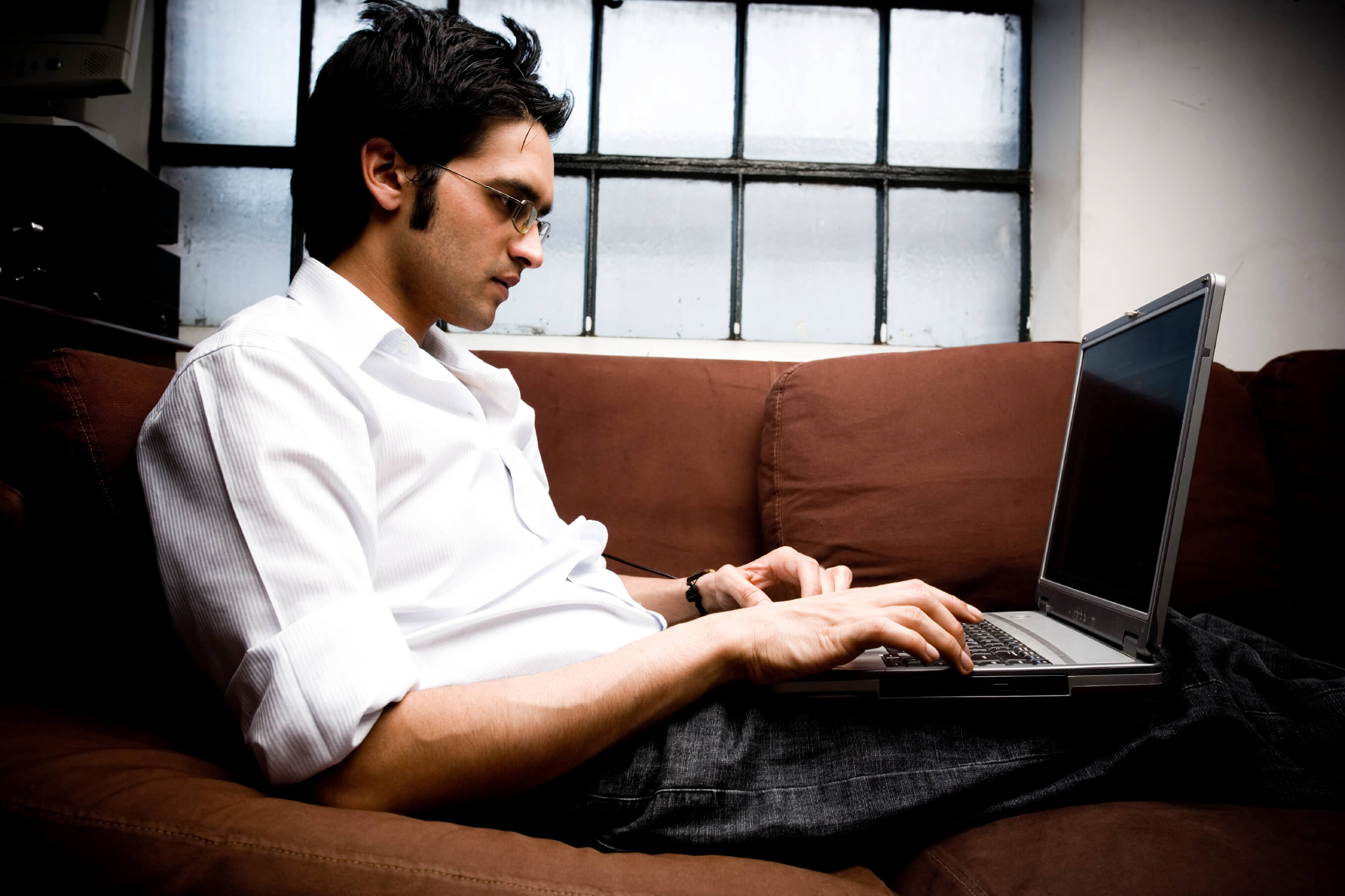 Man working on a laptop while laying on a couch